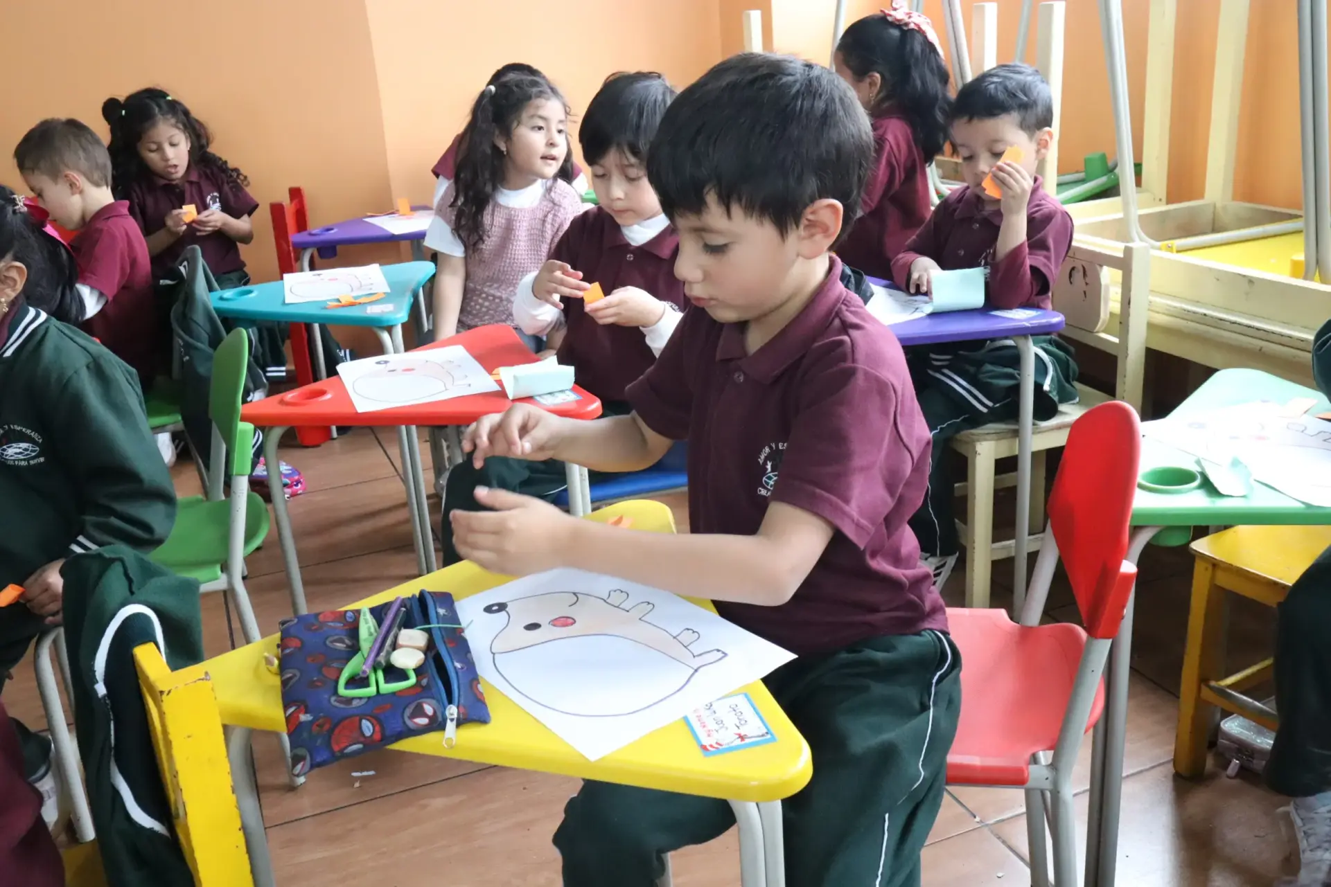 Niños pequeños realizando una actividad artística en el aula, recortando y pegando figuras en hojas de papel