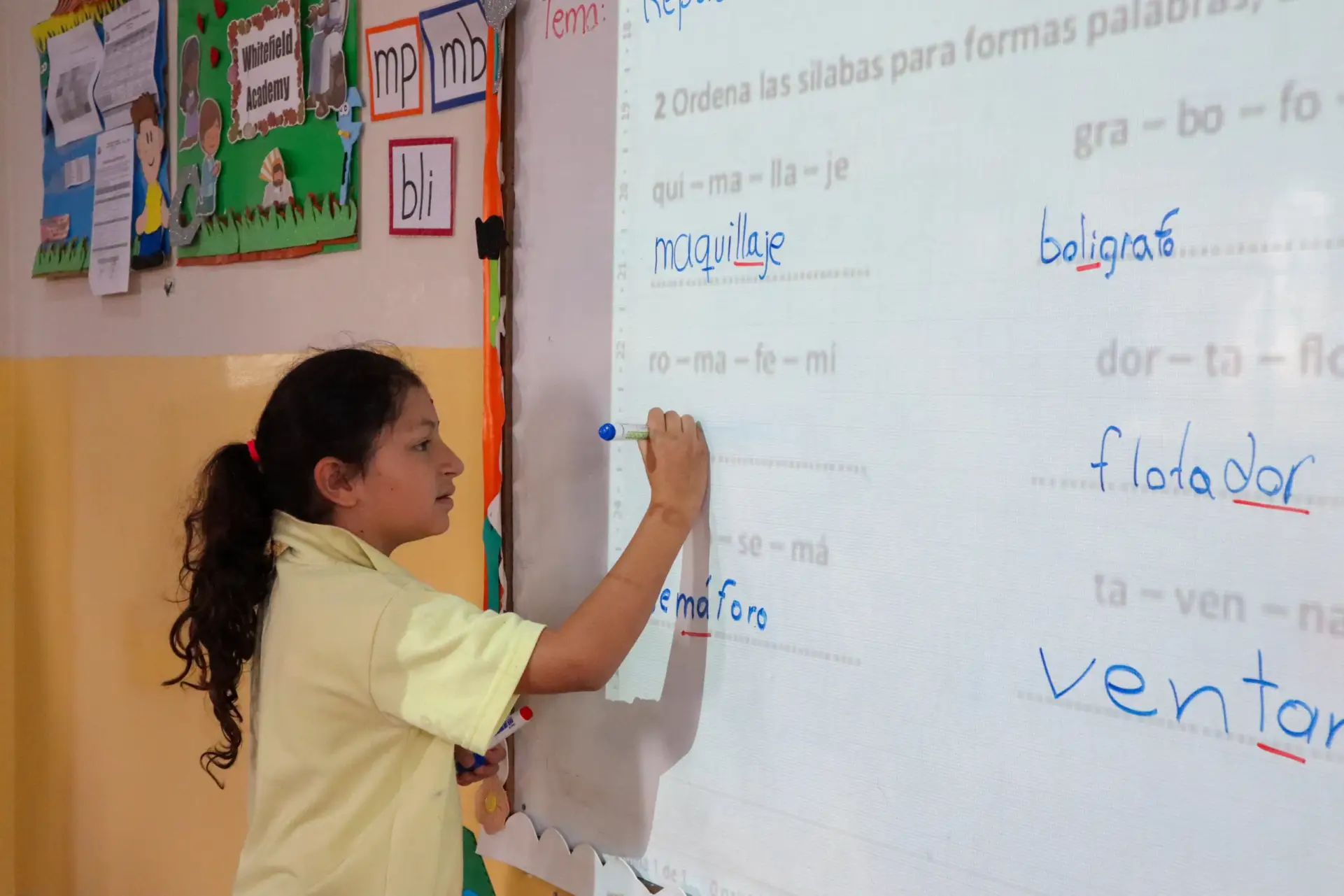 Niña de primaria realizando una actividad de lenguaje en el pizarrón frente a la clase.